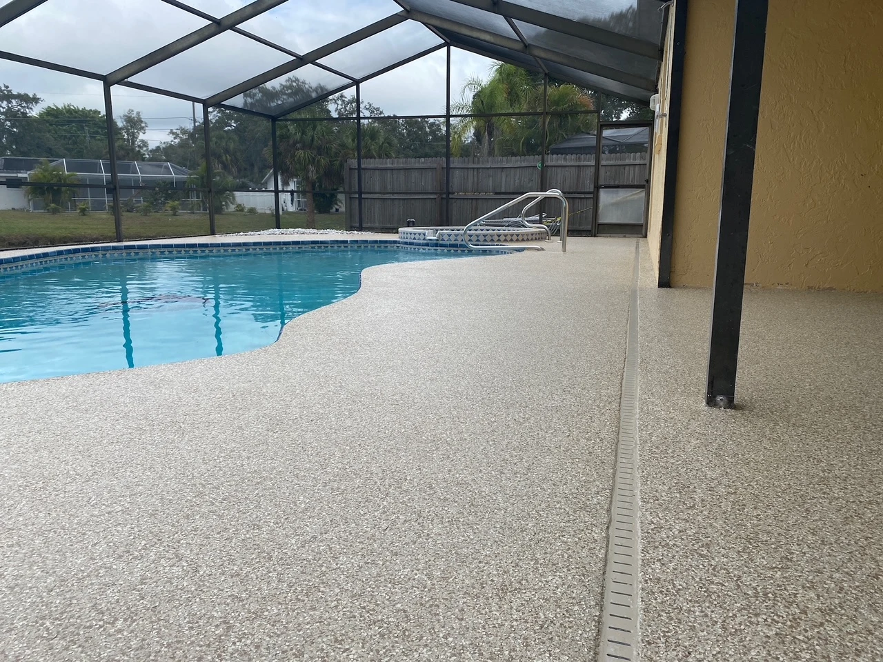 Newly refinished light flake pool deck inside a screened Florida lanai